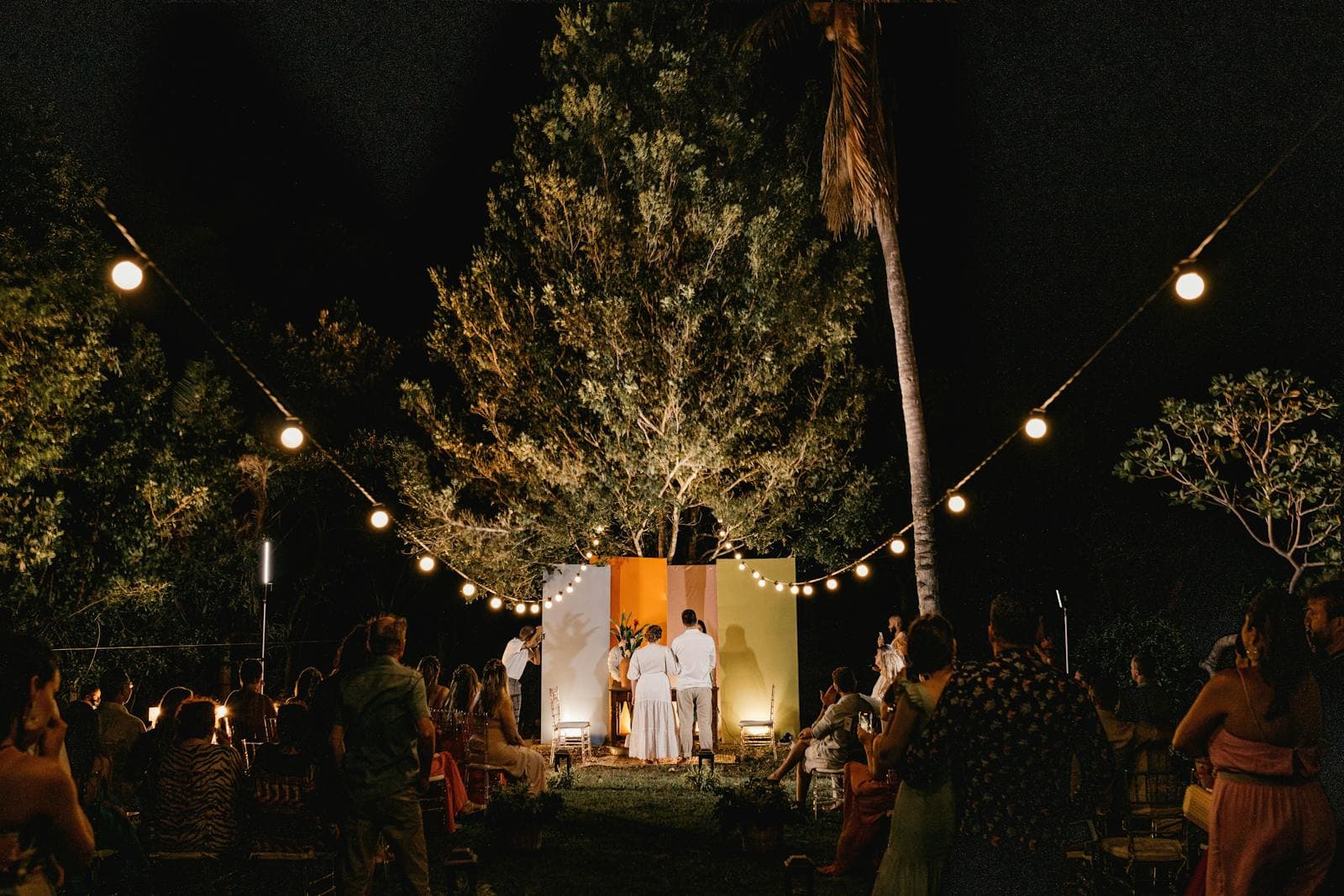 Sacramento backyard wedding reception illuminated by permanent outdoor LED lights with guests seated under string lighting at twilight